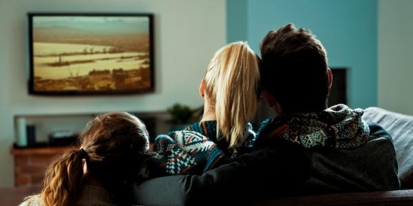 Družina sedi na kavču in skupaj gleda televizijo – tipičen primer, kako lahko ciljano TV oglaševanje v Sloveniji doseže želene ciljne skupine.