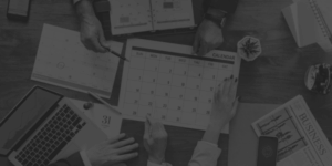 Ekipa pri mizi načrtuje koledar in strategijo za učinkovito oglaševanje s pomočjo poslovnih dokumentov, prenosnega računalnika in revij.