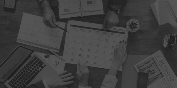 Ekipa pri mizi načrtuje koledar in strategijo za učinkovito oglaševanje s pomočjo poslovnih dokumentov, prenosnega računalnika in revij.